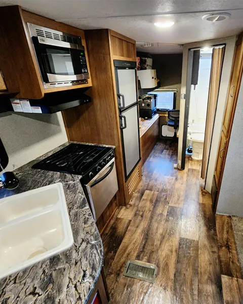 The image shows the same space as the prior photo. All of the spaces have been cleaned. The sink, countertop, and stove are clean. The floor is shining wood.