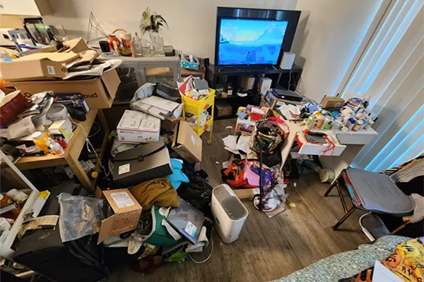 A before photo of a living space. A kitchen counter and living room space with accessibility and access issues due to an accumulation of items.
