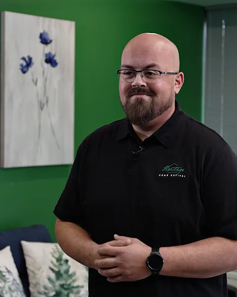 Brandon stands in front of a green wall in the Heritage offices. He has a pleasant expression on his face.