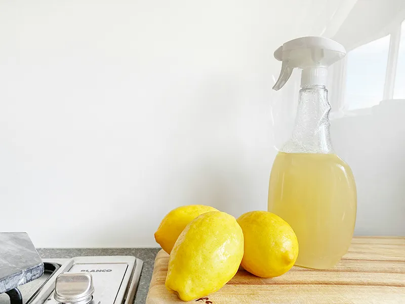 Three lemons and a spray bottle of cleaner sit on a kitchen counter next to stove controls