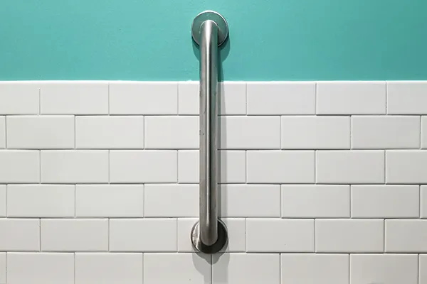 A grab bar installed on white tile and an aqua wall.