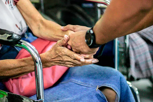 A person sitting in a wheelchair holds hands with someone standing. This is a close up photo of their hands